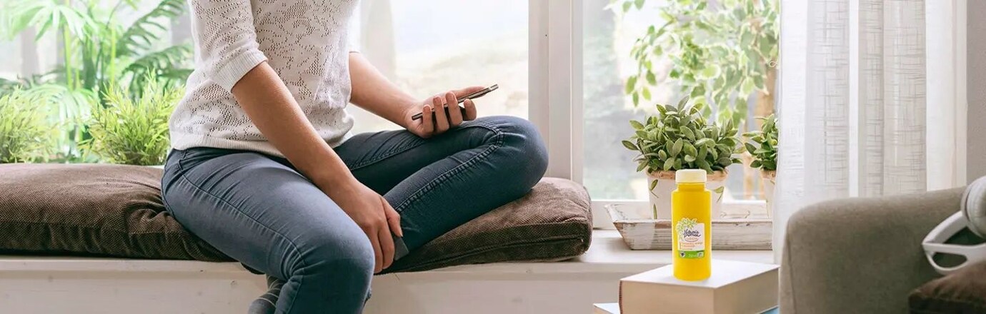 žena sedící na okně s mobilem v ruce a na stole má šťávu z ovoce